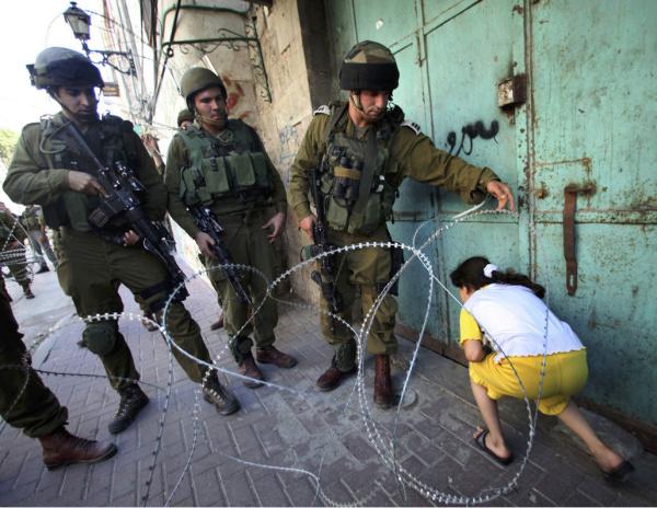 Israeli soldiers let a Palestinian girl make her way past a barbed wire barricade set up to prevent protesting Palestinians from accessing an Israeli settlement, in Hebron on the West Bank.